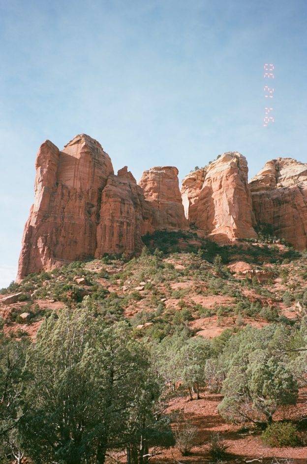 Red rock formations with green trees under a blue sky.